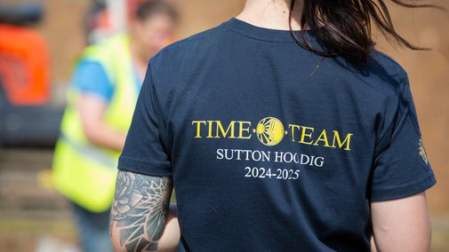A woman wearing a navy blue coloured tee-shirt with the Time Team logo and 'Sutton Hoo 2025-2025' written on the back of it
